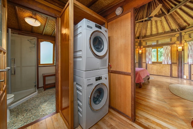 clothes washing area featuring stacked washer / dryer, wood walls, and light wood-type flooring