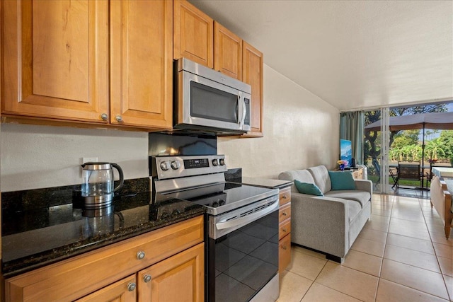 kitchen featuring stainless steel appliances, expansive windows, dark stone countertops, and light tile patterned floors