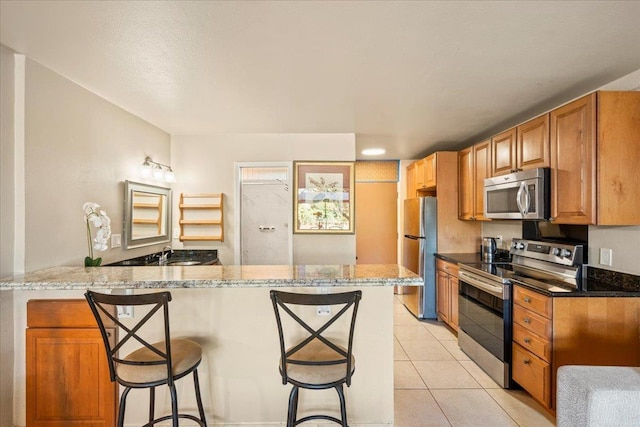 kitchen with a breakfast bar, light tile patterned floors, kitchen peninsula, stainless steel appliances, and light stone countertops