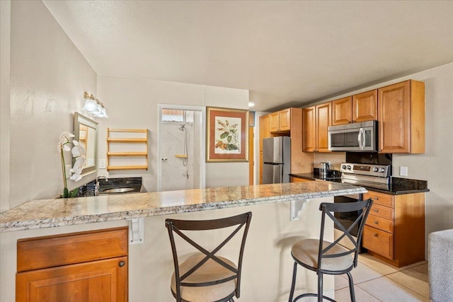 kitchen with sink, appliances with stainless steel finishes, light stone countertops, a kitchen bar, and kitchen peninsula