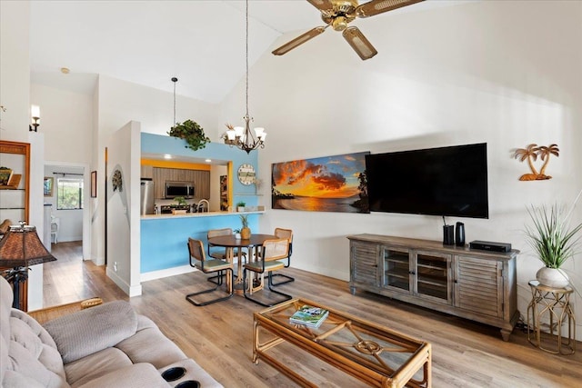 living room with high vaulted ceiling, light hardwood / wood-style flooring, and ceiling fan with notable chandelier