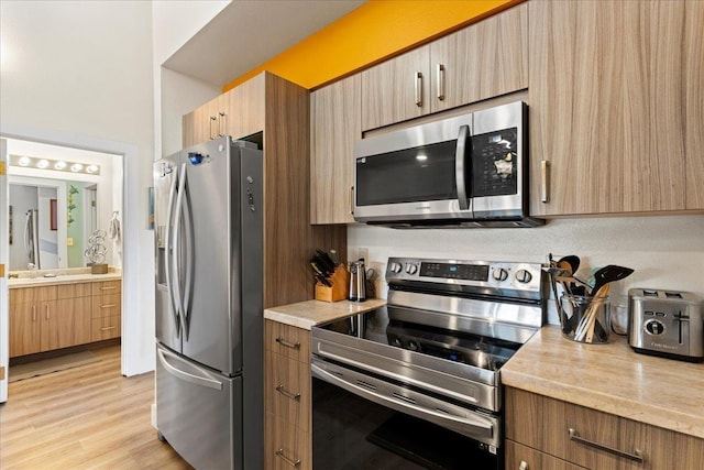 kitchen with stainless steel appliances, light hardwood / wood-style floors, and light stone countertops