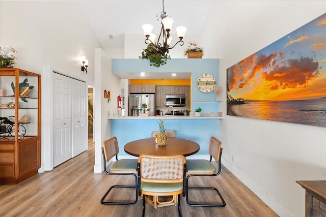 dining area with high vaulted ceiling, a notable chandelier, and light hardwood / wood-style flooring