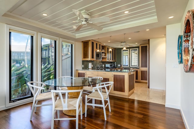 dining area featuring light hardwood / wood-style floors, a raised ceiling, ceiling fan, and sink