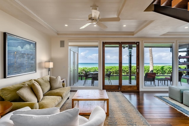 living room featuring a tray ceiling, ceiling fan, a water view, and dark hardwood / wood-style floors