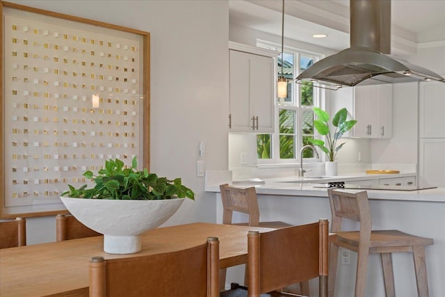 kitchen with white cabinetry, island range hood, sink, decorative light fixtures, and a breakfast bar area