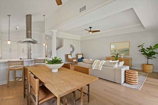 dining space with decorative columns, ceiling fan, light hardwood / wood-style floors, and a tray ceiling