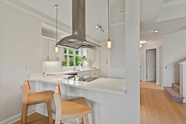 kitchen featuring kitchen peninsula, decorative light fixtures, white cabinetry, a kitchen bar, and island range hood