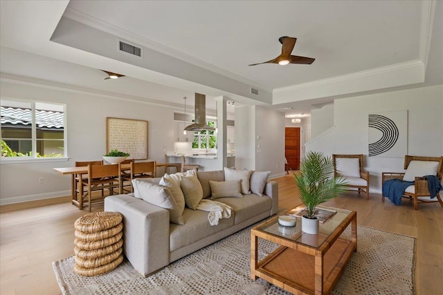 living room with ceiling fan, a tray ceiling, ornamental molding, and light wood-type flooring