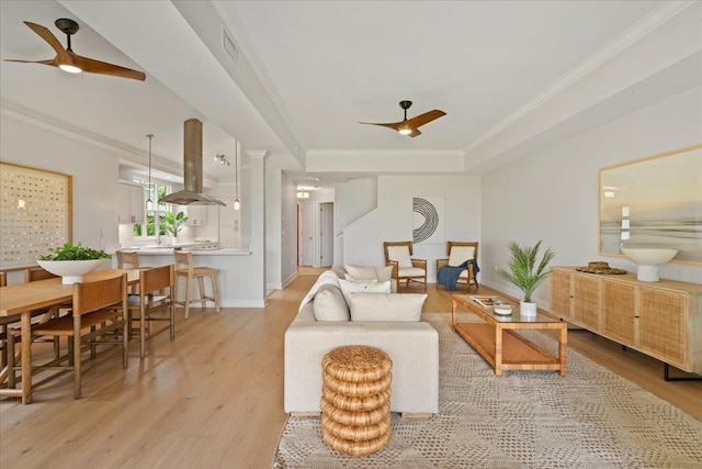 living room featuring a tray ceiling, ceiling fan, light hardwood / wood-style flooring, and crown molding