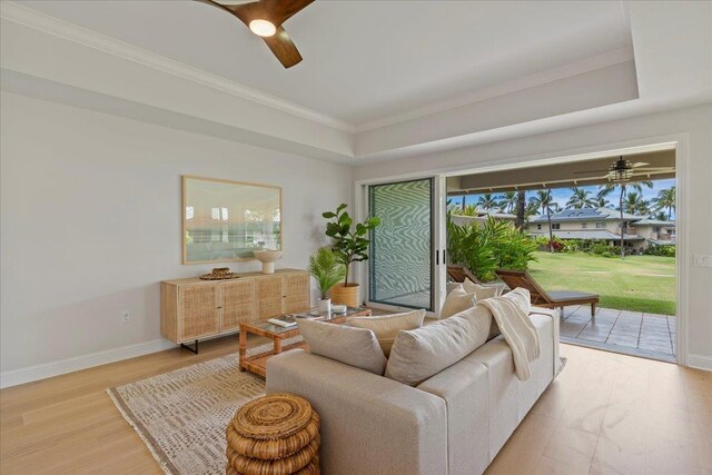 living room featuring ceiling fan, a tray ceiling, ornamental molding, and light wood-type flooring