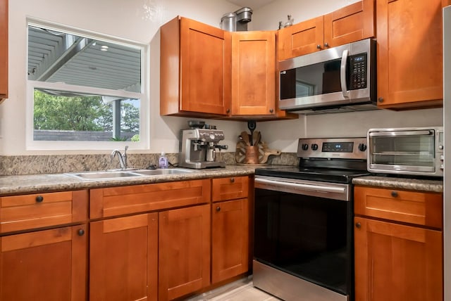 kitchen with a sink, stainless steel appliances, brown cabinetry, and a toaster