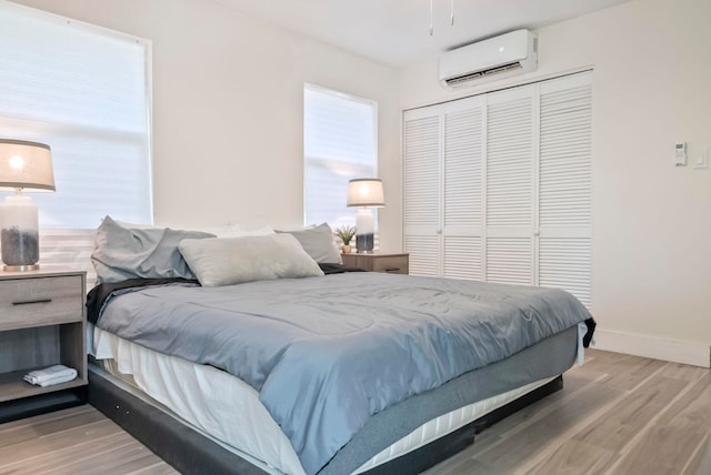 bedroom featuring a wall mounted AC, baseboards, a closet, and wood finished floors