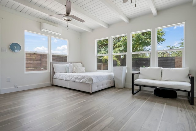 bedroom featuring multiple windows, beamed ceiling, a wall unit AC, and light wood-style floors