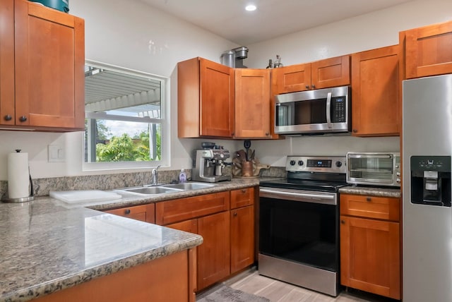 kitchen with a sink, appliances with stainless steel finishes, brown cabinetry, and a toaster