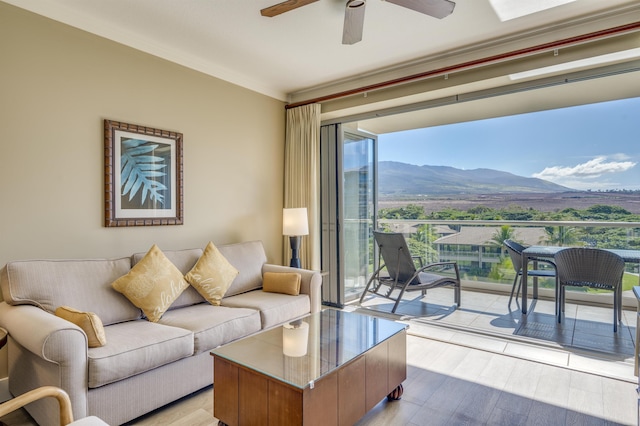 living room featuring a mountain view, light hardwood / wood-style flooring, ceiling fan, and ornamental molding