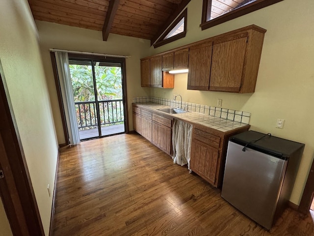 kitchen featuring sink, wood ceiling, stainless steel refrigerator, vaulted ceiling with beams, and tile countertops