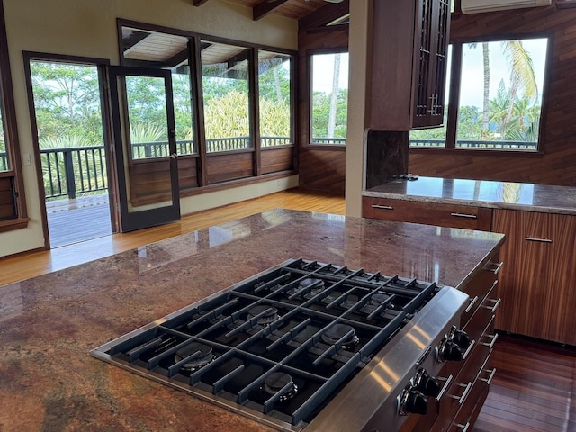 kitchen with a wall unit AC, stovetop, dark stone countertops, and dark hardwood / wood-style flooring