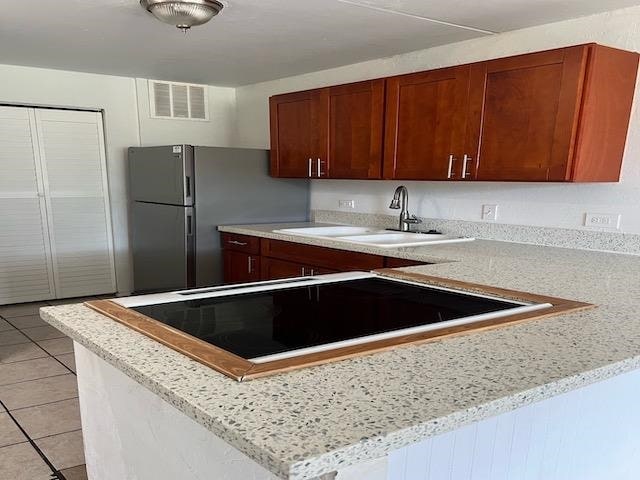 kitchen featuring stainless steel refrigerator, light stone countertops, sink, kitchen peninsula, and light tile patterned floors