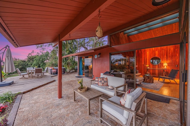 patio terrace at dusk featuring outdoor dining space, an outdoor hangout area, and a wooden deck