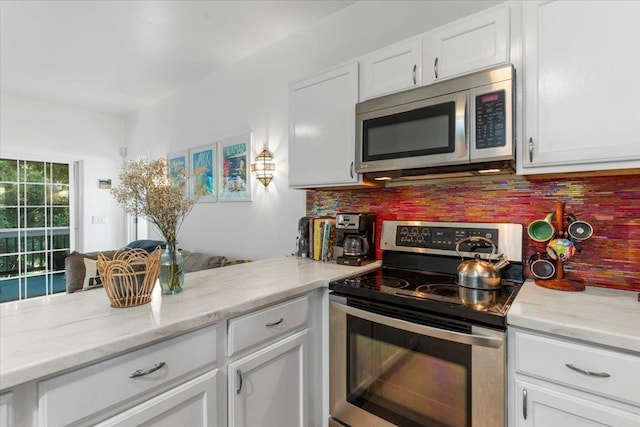 kitchen featuring light stone counters, backsplash, kitchen peninsula, white cabinets, and appliances with stainless steel finishes