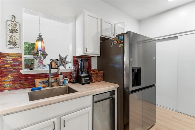 kitchen featuring stainless steel refrigerator with ice dispenser, sink, light hardwood / wood-style floors, white cabinetry, and hanging light fixtures