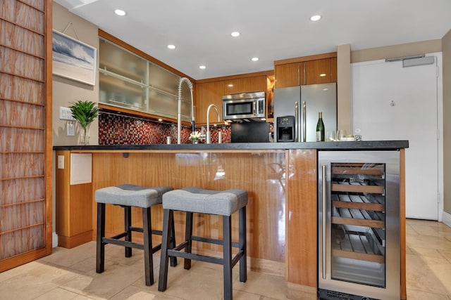 kitchen with appliances with stainless steel finishes, a breakfast bar, wine cooler, backsplash, and kitchen peninsula