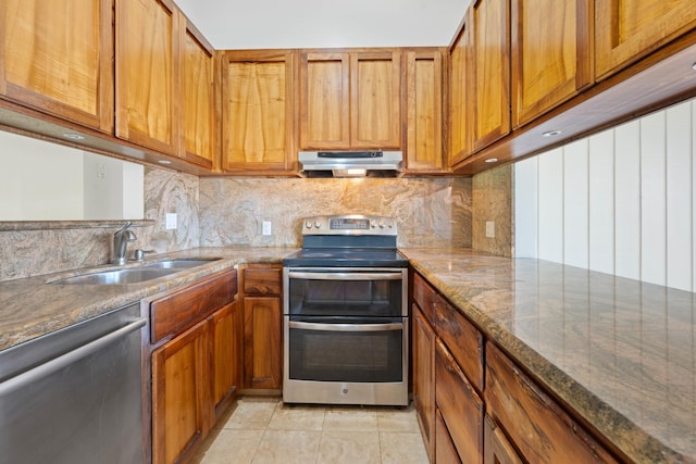 kitchen with under cabinet range hood, brown cabinetry, appliances with stainless steel finishes, and a sink