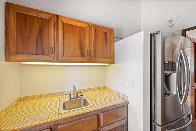 kitchen featuring a sink, stainless steel fridge, brown cabinets, and light countertops