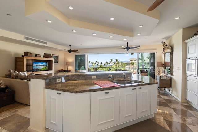 kitchen featuring a center island with sink, white cabinetry, white oven, dark stone counters, and sink