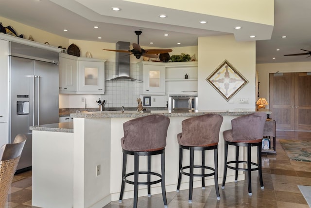 kitchen with white cabinets, a large island, wall chimney range hood, built in fridge, and a kitchen breakfast bar