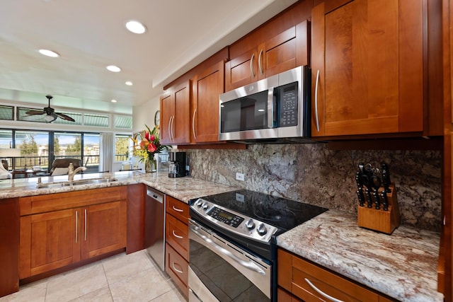 kitchen featuring ceiling fan, light stone counters, sink, stainless steel appliances, and decorative backsplash