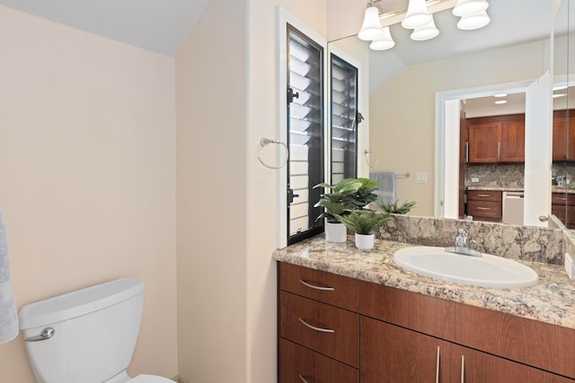 bathroom with vanity, toilet, vaulted ceiling, and tasteful backsplash