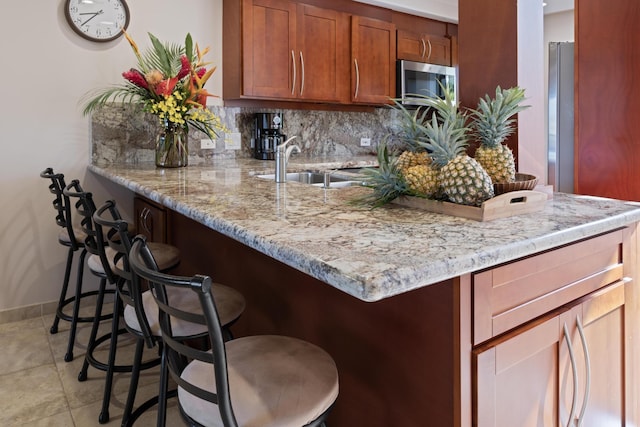 100 Ridge Rd Unit 723, Lahaina, HI 96761 - kitchen with a breakfast bar, light stone counters, a peninsula, appliances with stainless steel finishes, and brown cabinets