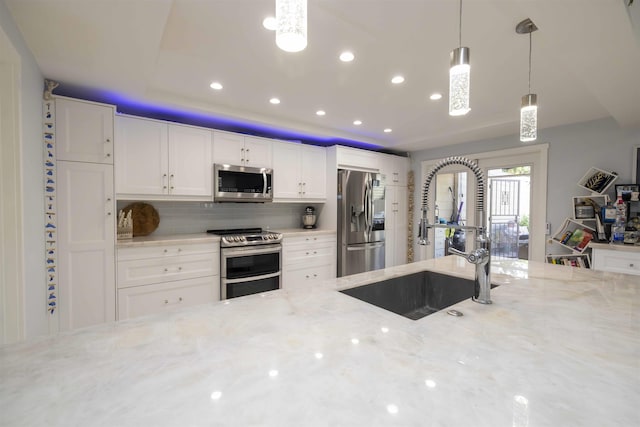 kitchen featuring a sink, appliances with stainless steel finishes, light stone counters, and hanging light fixtures