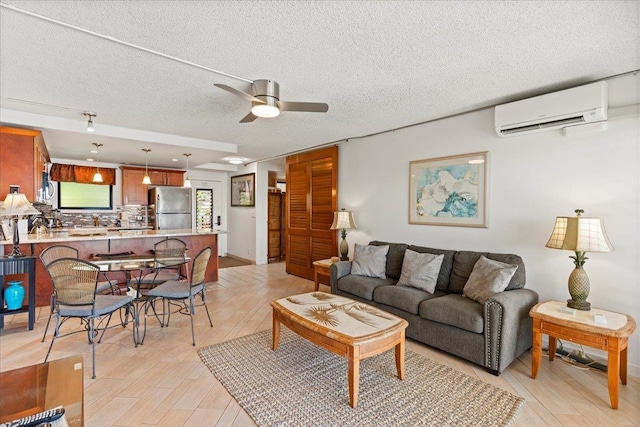 living room featuring a wall mounted air conditioner, ceiling fan, light hardwood / wood-style flooring, and a textured ceiling