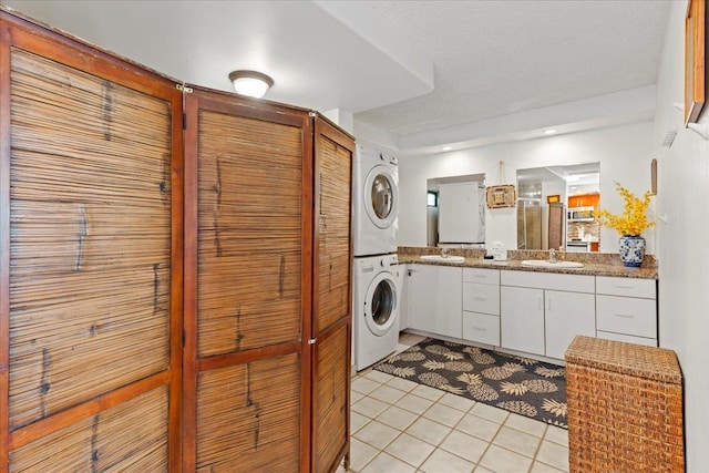 laundry room featuring sink, a textured ceiling, light tile patterned floors, and stacked washer / drying machine