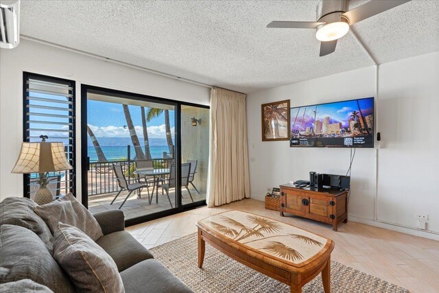 living room with a textured ceiling, light hardwood / wood-style flooring, ceiling fan, and a wall unit AC