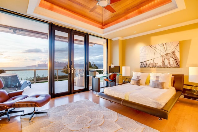 bedroom featuring ornamental molding, access to outside, a tray ceiling, ceiling fan, and a water view