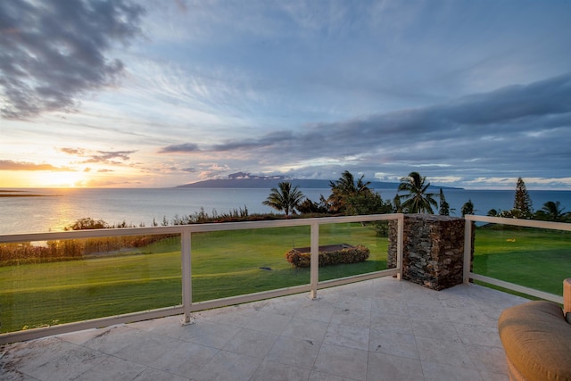 patio terrace at dusk featuring a water view and a lawn