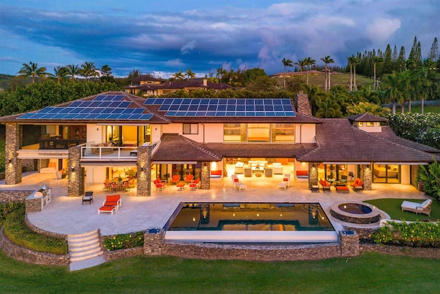 back house at dusk featuring a patio area, an outdoor living space, a swimming pool with hot tub, and a balcony