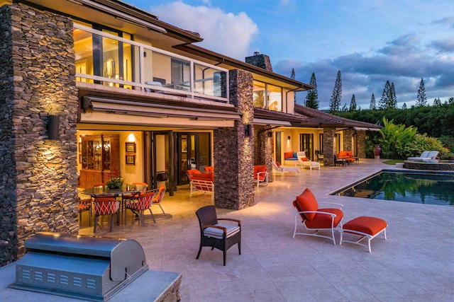 back house at dusk featuring a patio area, a balcony, and area for grilling