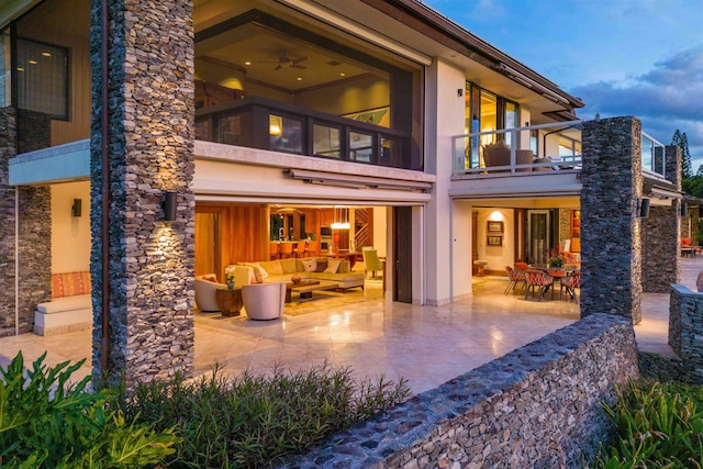 back house at dusk featuring an outdoor living space, a balcony, and a patio