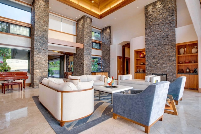 living room with built in shelves, a stone fireplace, and a high ceiling