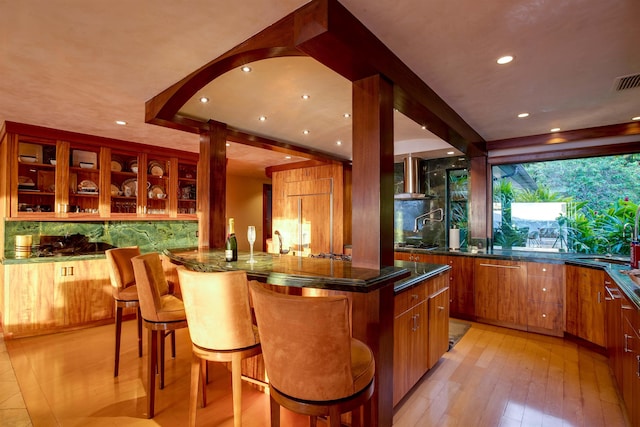 bar featuring stainless steel gas stovetop, wall chimney exhaust hood, and light wood-type flooring