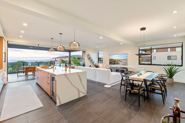 kitchen with light stone countertops, beverage cooler, pendant lighting, light brown cabinets, and a center island with sink