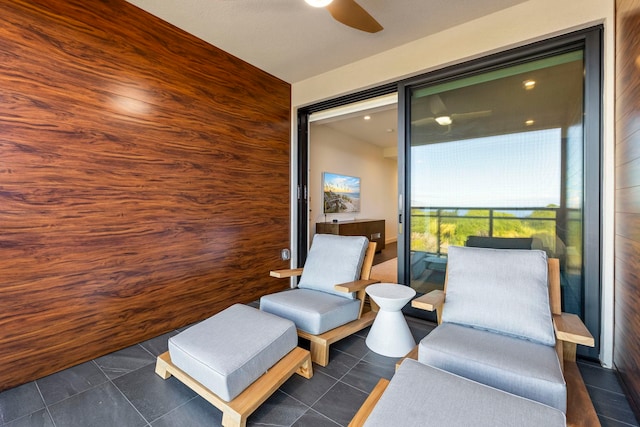 living area with ceiling fan, dark tile patterned floors, and wooden walls