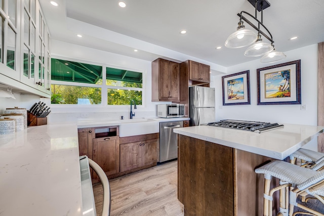 kitchen featuring sink, stainless steel appliances, pendant lighting, light hardwood / wood-style floors, and a breakfast bar