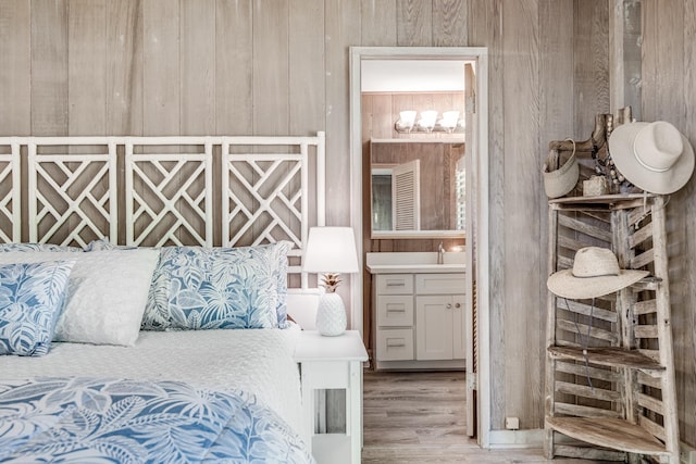 bedroom with ensuite bath, wooden walls, sink, and light wood-type flooring