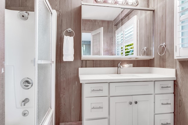 bathroom featuring shower / bath combination with glass door, wood walls, and vanity